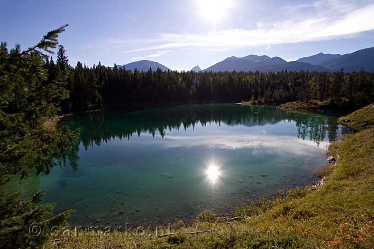 De weerspiegeling van de zon, de bomen en de bergen in Fourth Lake